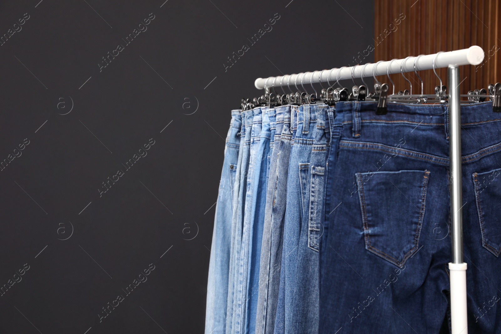 Photo of Rack with different jeans on dark grey background. Space for text