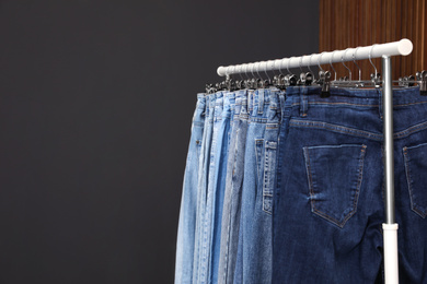 Photo of Rack with different jeans on dark grey background. Space for text