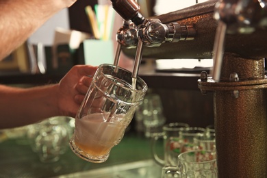 Photo of Bartender pouring beer from tap into glass in bar, closeup
