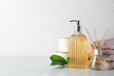 Stylish soap dispenser, air freshener, towels and leaves on light table. Space for text