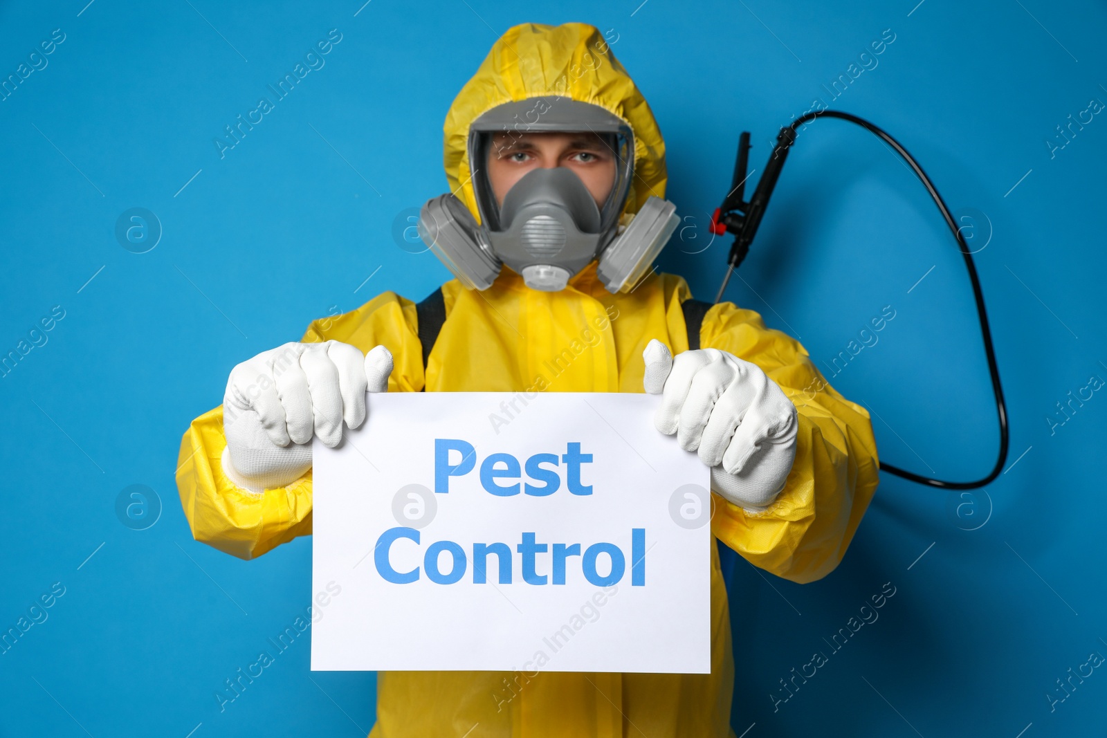 Photo of Man wearing protective suit with insecticide sprayer holding sign PEST CONTROL on blue background