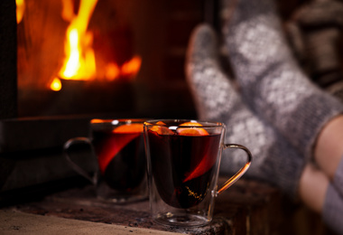 Photo of Tasty mulled wine in glass cups near fireplace indoors