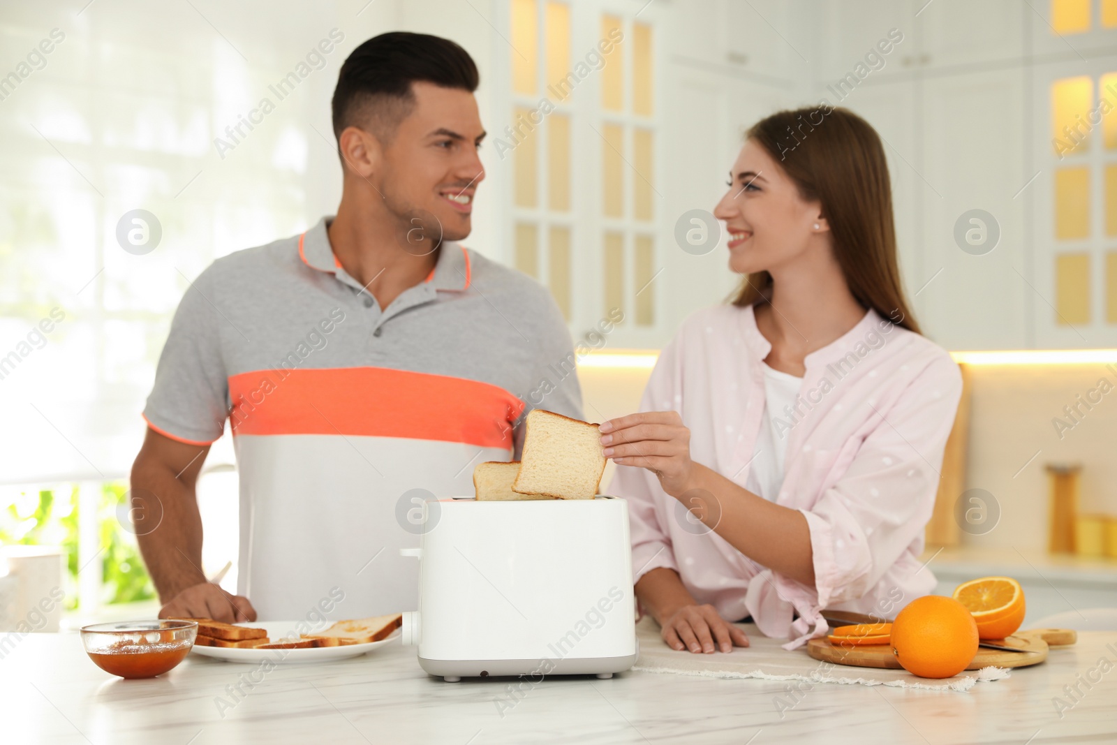 Photo of Happy couple preparing breakfast with toasted bread at table in kitchen