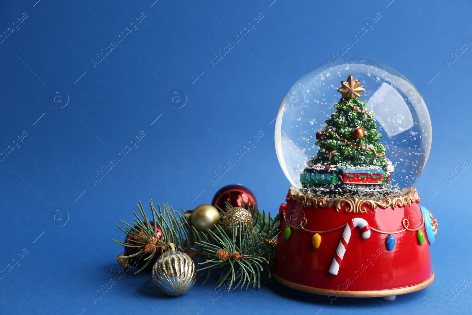 Photo of Beautiful snow globe, Christmas balls and fir branches on blue background, space for text