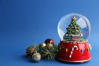 Beautiful snow globe, Christmas balls and fir branches on blue background, space for text