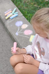 Little child chalk piece sitting on curb outdoors