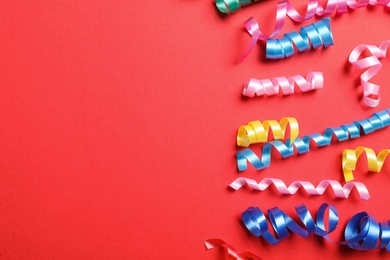 Colorful serpentine streamers on red background, flat lay. Space for text