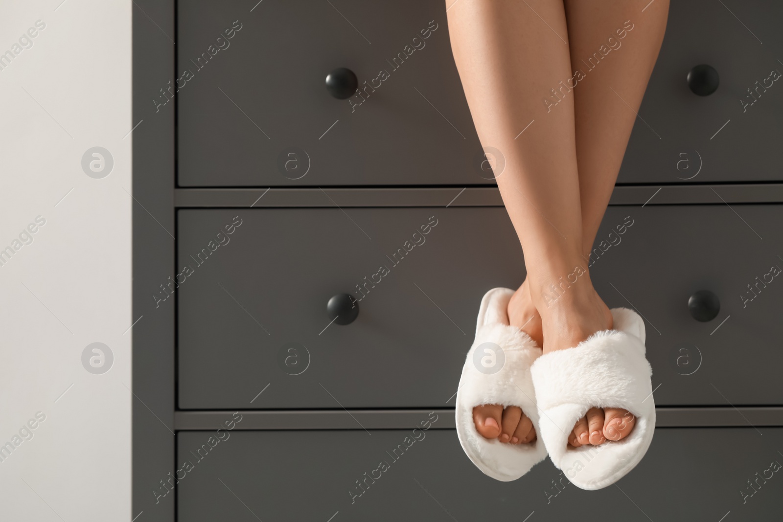 Photo of Woman in soft slippers sitting on chest of drawers, closeup