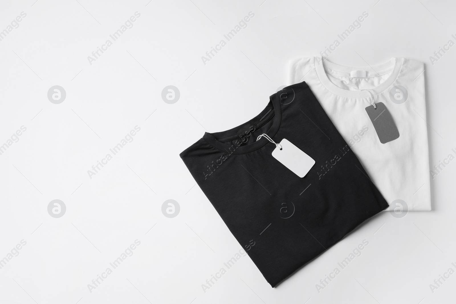 Photo of Stylish T-shirts with labels on white background, top view. Space for text