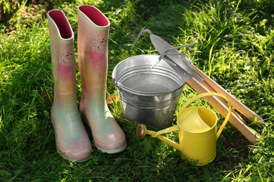 Photo of Watering can, gardening tools and rubber boots on green grass outdoors