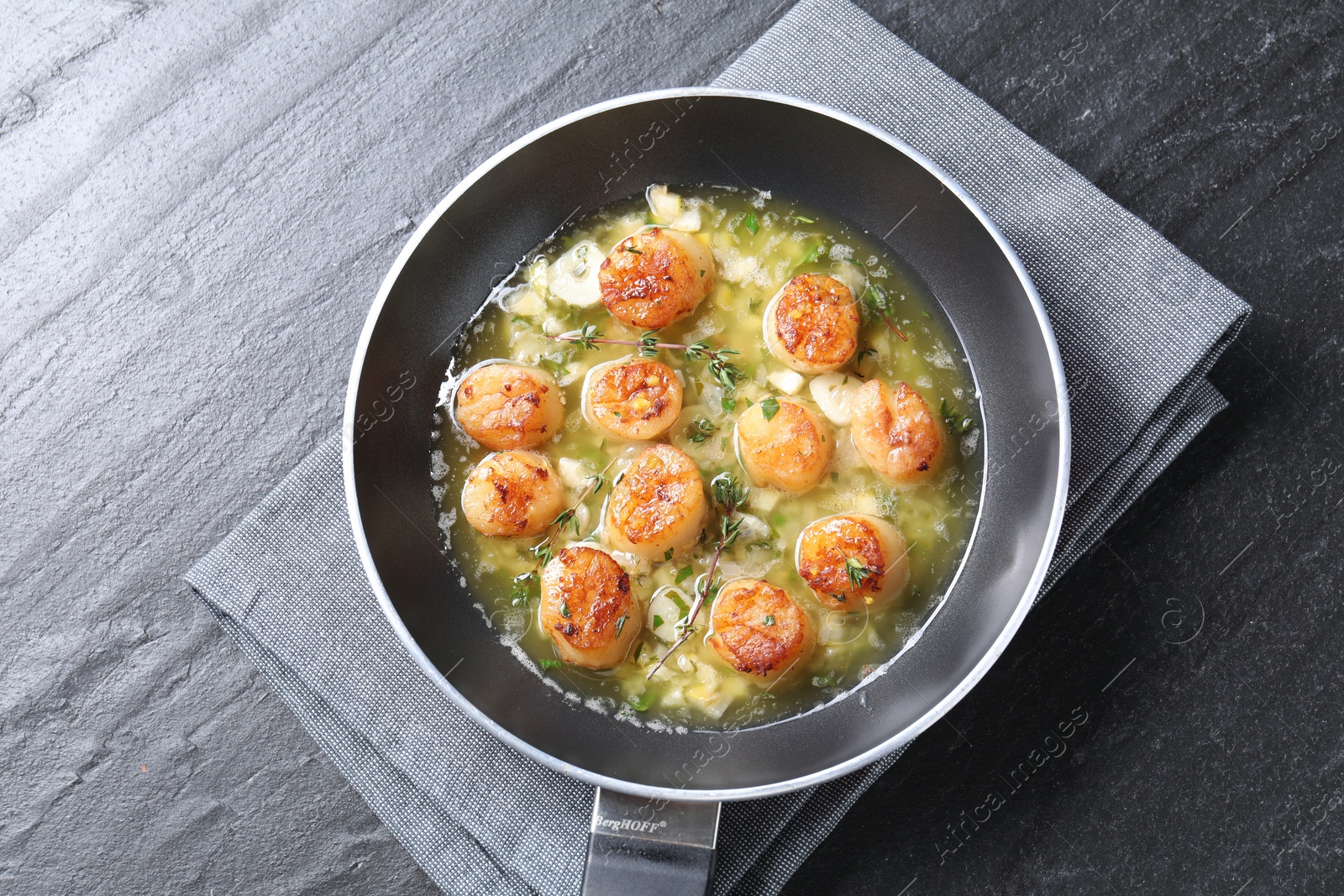 Photo of Delicious scallops with sauce in frying pan on dark gray textured table, top view