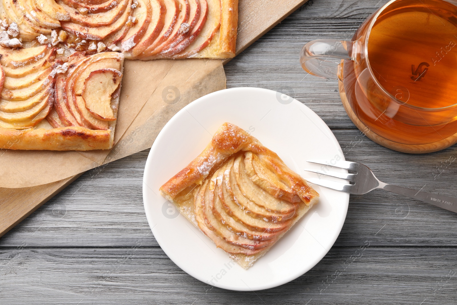 Photo of Tasty apple pie served with tea on grey wooden table, flat lay