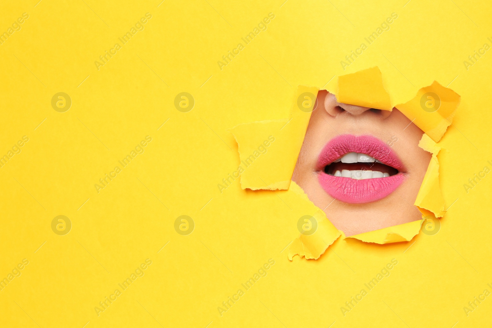 Photo of Lips of young woman with beautiful lipstick visible through hole in color paper. Space for text