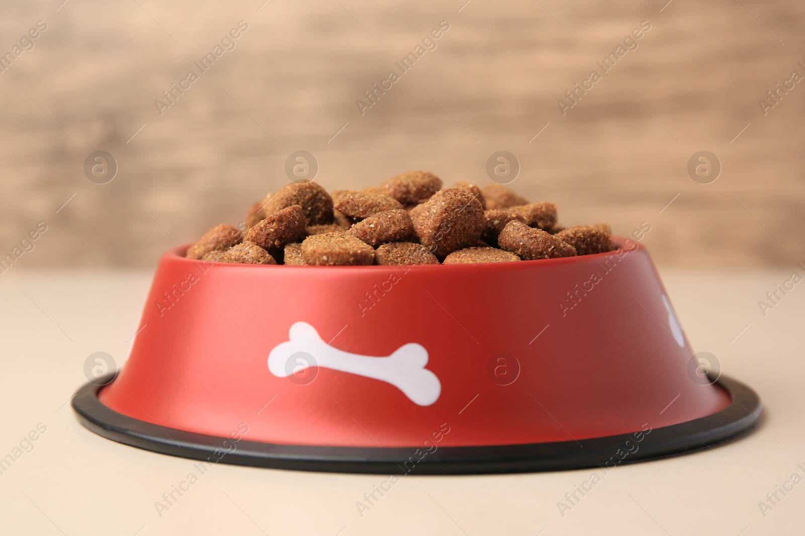 Photo of Dry dog food in feeding bowl on beige table