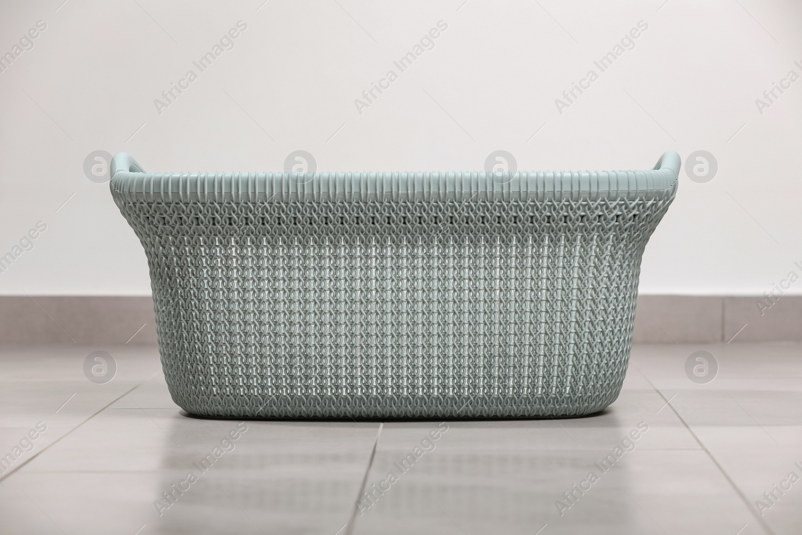 Photo of Empty plastic laundry basket on floor near white wall