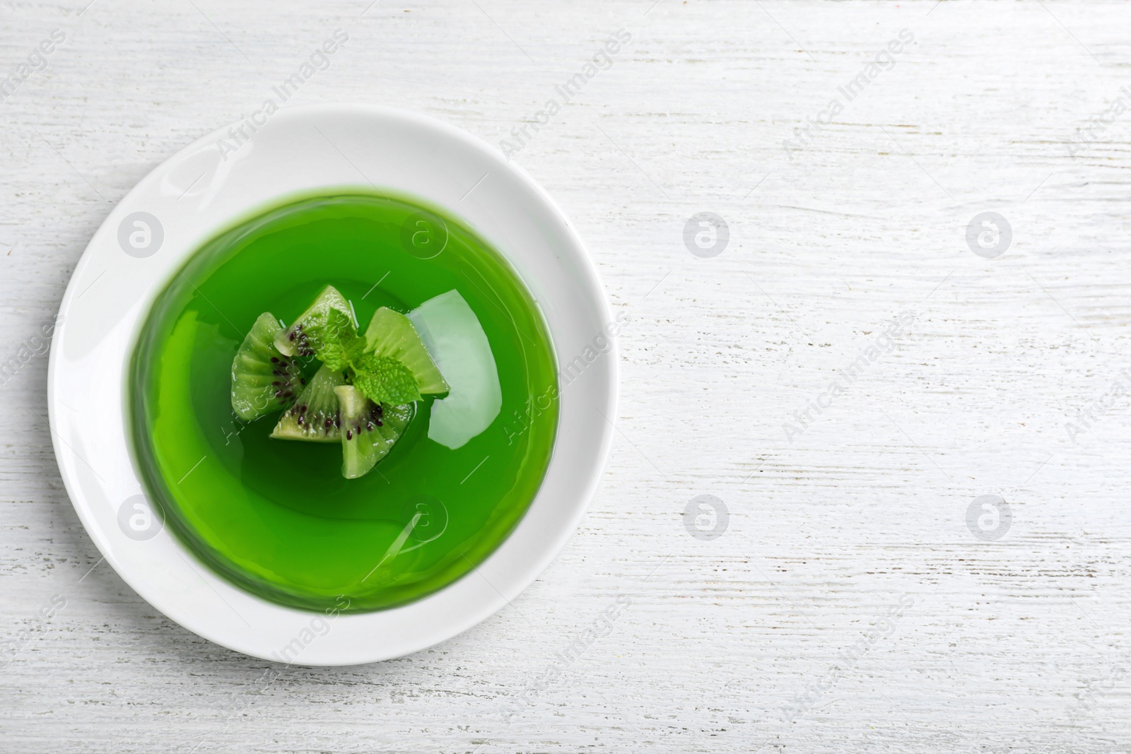 Photo of Delicious green jelly with kiwi slices on white wooden table, top view. Space for text