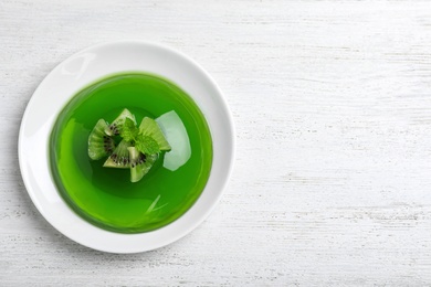 Delicious green jelly with kiwi slices on white wooden table, top view. Space for text