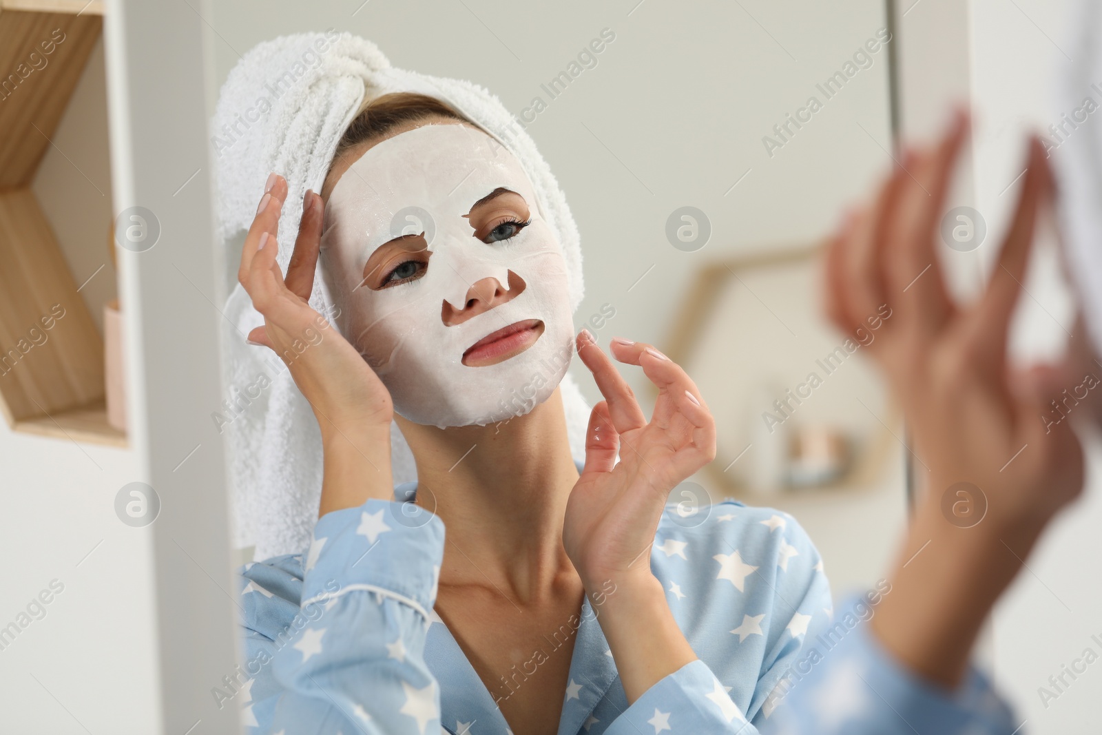 Photo of Young woman with face mask looking into mirror indoors. Spa treatments
