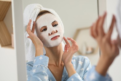 Young woman with face mask looking into mirror indoors. Spa treatments