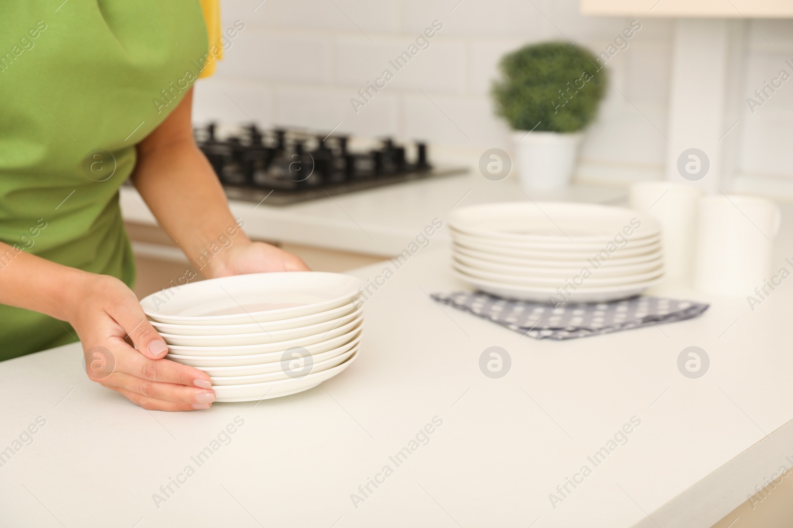 Photo of Woman with stack of clean dishes in kitchen, closeup