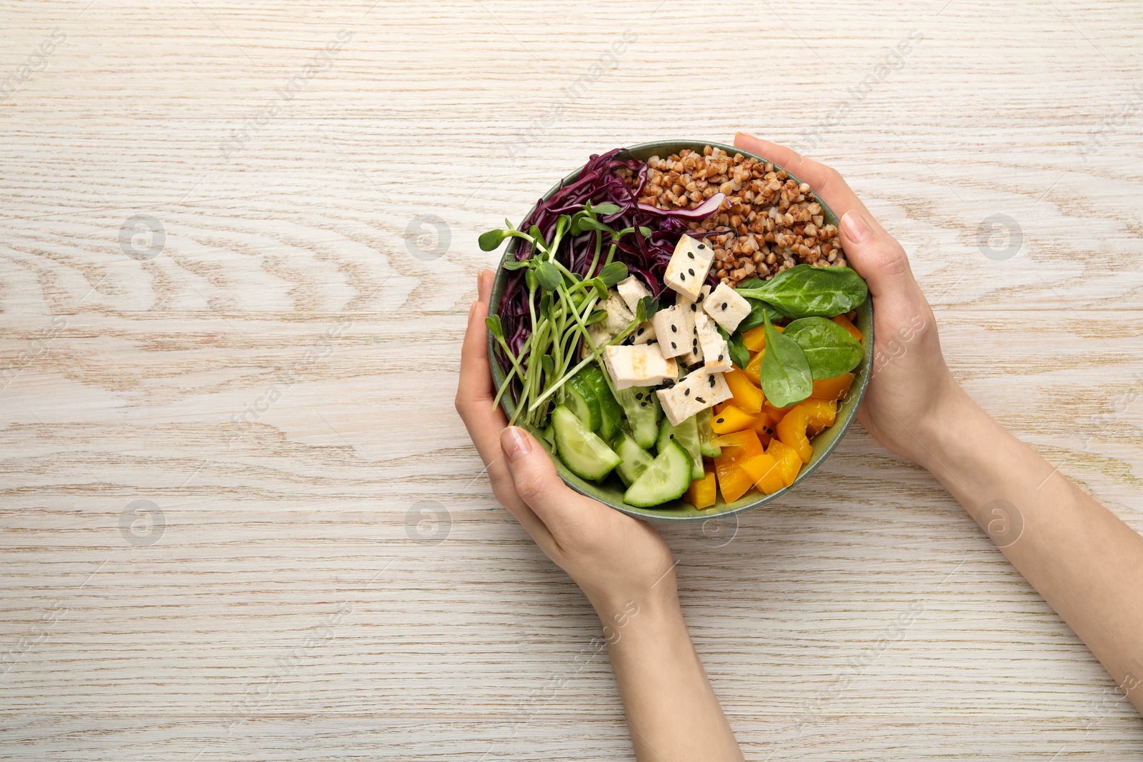 Photo of Woman holding delicious vegan bowl with tomatoes, microgreens and buckwheat at white wooden table, top view. Space for text