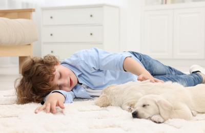 Photo of Little boy lying with cute puppies on white carpet at home