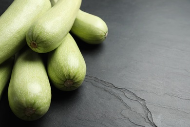 Photo of Raw green zucchinis on black slate table, closeup. Space for text