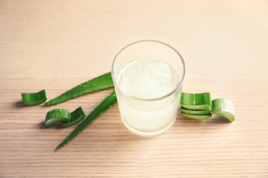 Photo of Glass with aloe vera juice and green leaves on wooden table