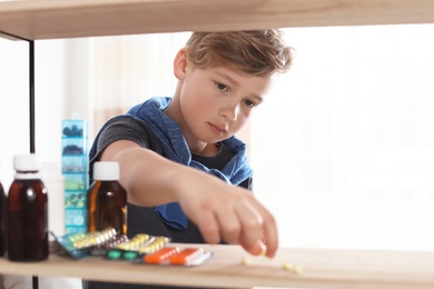 Little child taking pills from shelf at home. Danger of medicament intoxication