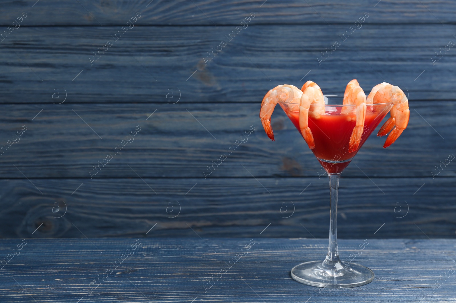 Photo of Shrimp cocktail with tomato sauce on blue wooden table. Space for text