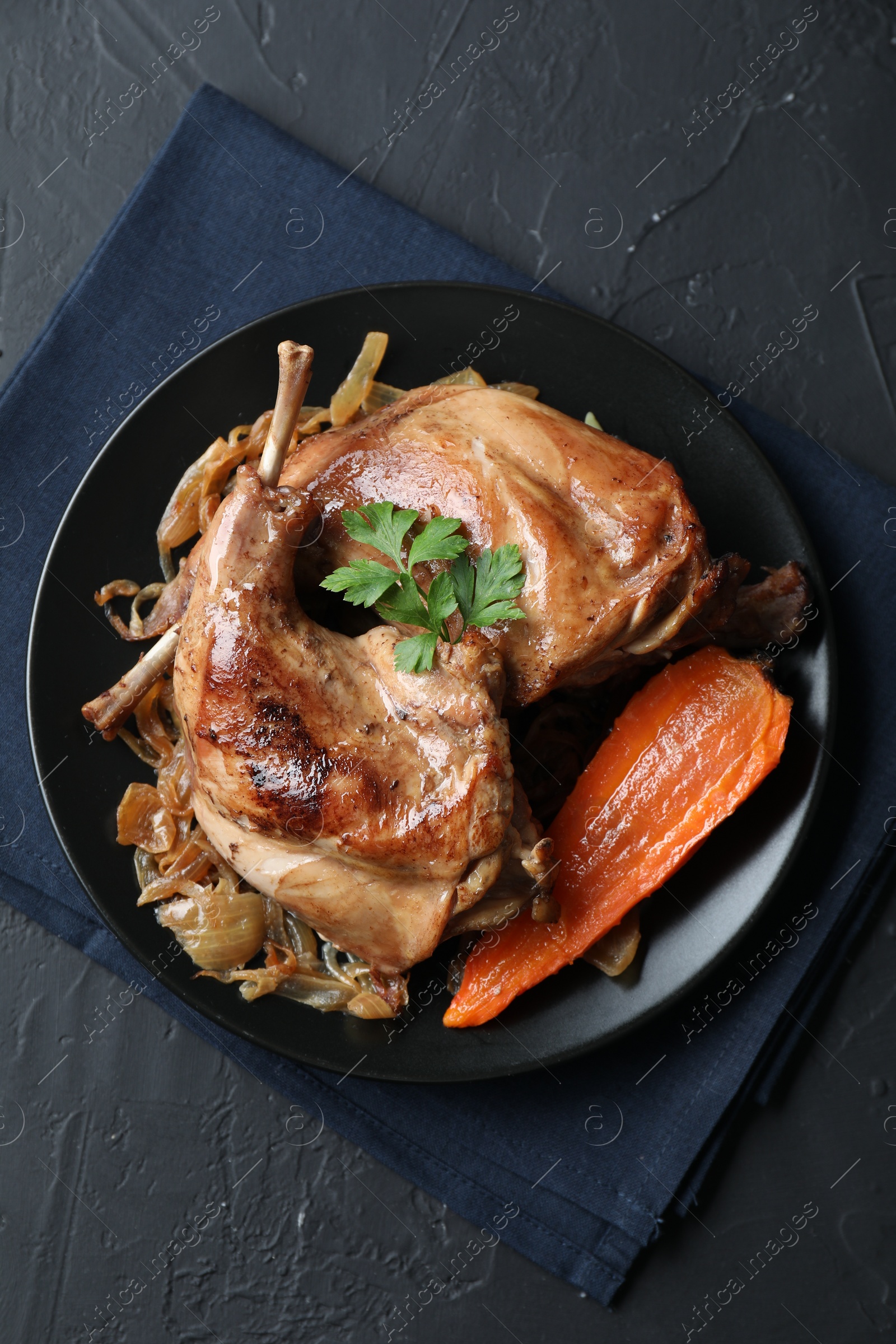 Photo of Tasty cooked rabbit meat with vegetables and parsley on black table, top view