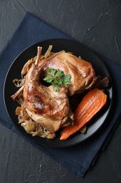 Tasty cooked rabbit meat with vegetables and parsley on black table, top view