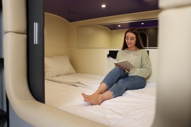 Photo of Happy young woman reading book in capsule of pod hostel