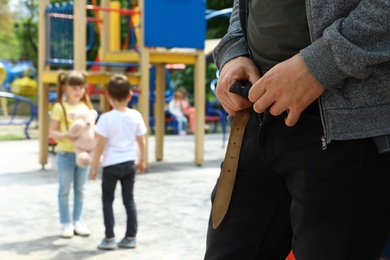 Photo of Suspicious adult man taking off his pants at playground with little kids, space for text. Child in danger