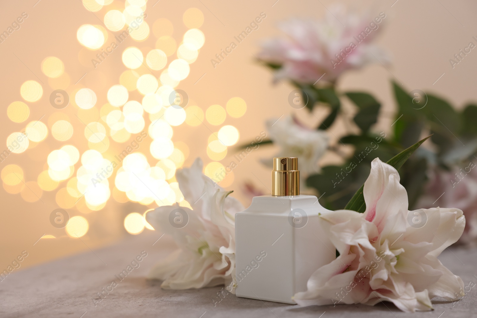 Photo of Bottle of perfume and beautiful lily flowers on table against beige background with blurred lights, closeup. Space for text