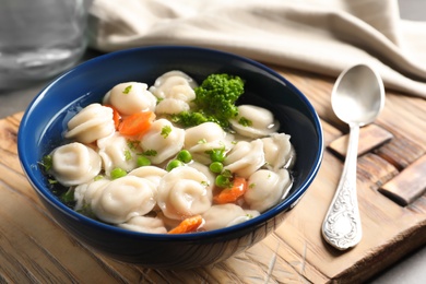 Photo of Board with bowl of dumplings in broth and spoon on table