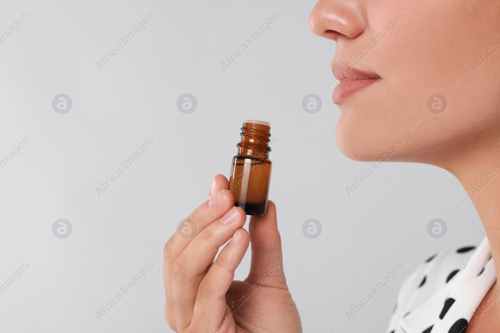 Photo of Woman with bottle of essential oil on light grey background, closeup