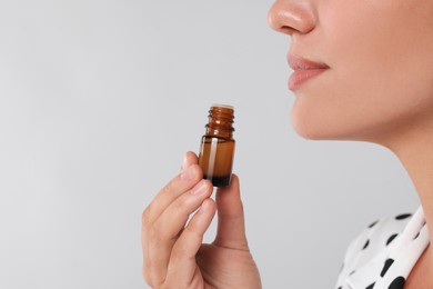 Woman with bottle of essential oil on light grey background, closeup
