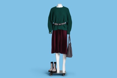 Photo of Female mannequin with bag and boots dressed in dark green sweater and skirt on light blue background