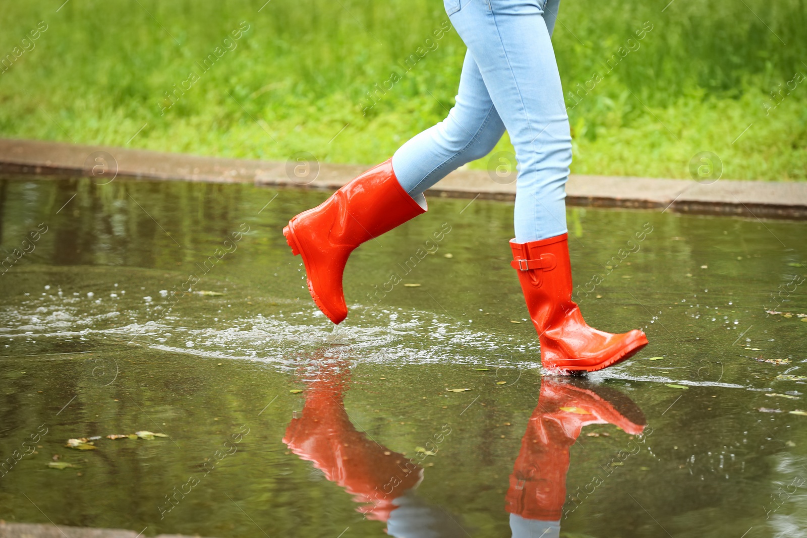 Photo of Woman with red rubber boots running in puddle, closeup. Rainy weather