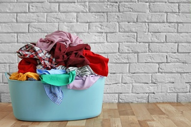 Photo of Laundry basket with dirty clothes on floor near brick wall