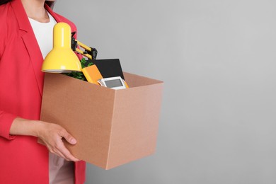 Photo of Unemployed woman with box of personal office belongings on grey background, closeup. Space for text