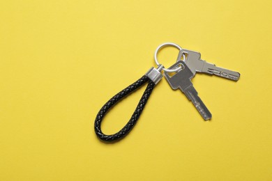 Photo of Keys with black leather keychain on yellow background, top view. Space for text