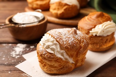 Photo of Delicious profiteroles with cream filling and powdered sugar on wooden table, closeup