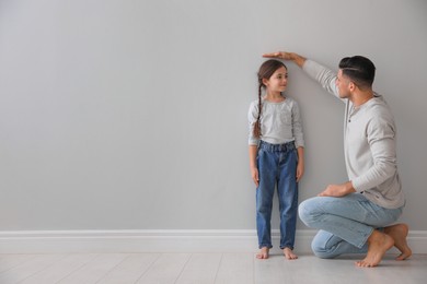 Photo of Father measuring little girl's height near light grey wall indoors. Space for text