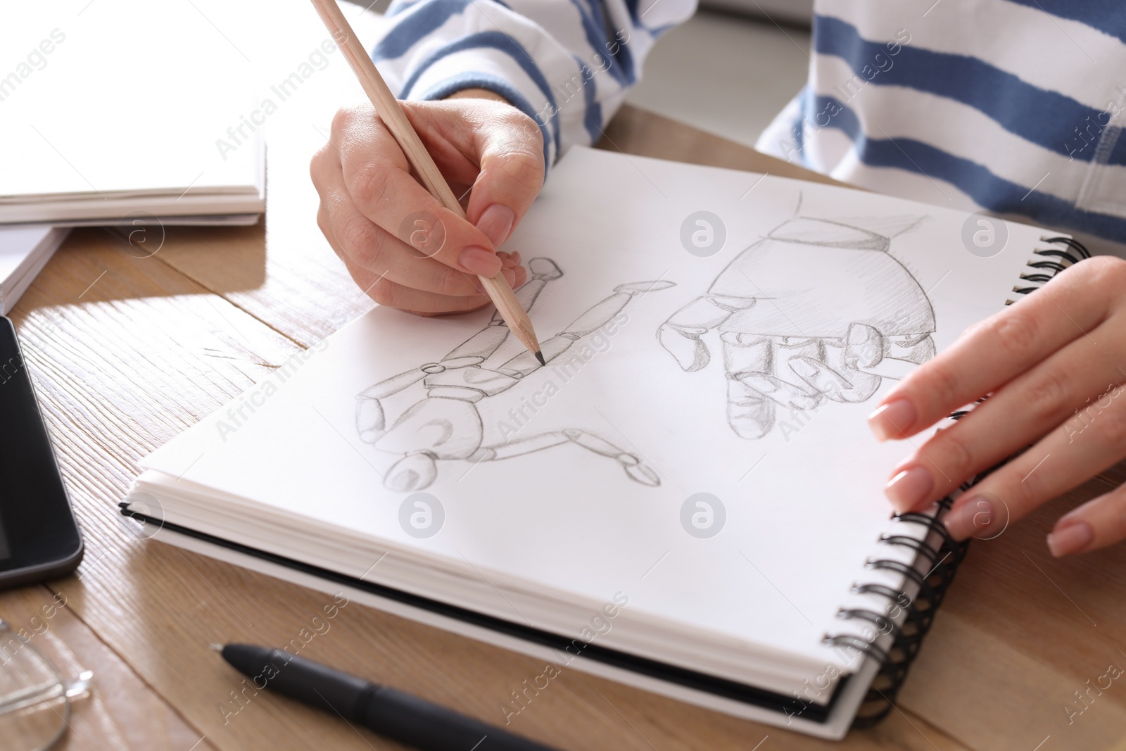 Photo of Woman drawing in sketchbook with pencil at wooden table, closeup