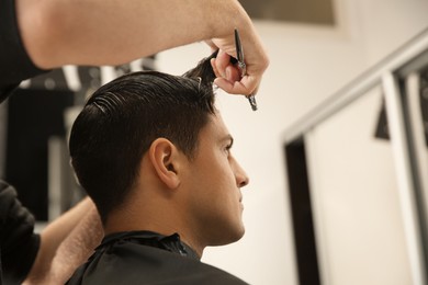 Photo of Professional barber making stylish haircut in salon, closeup. Space for text