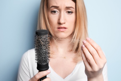 Young woman with hair loss problem on color background