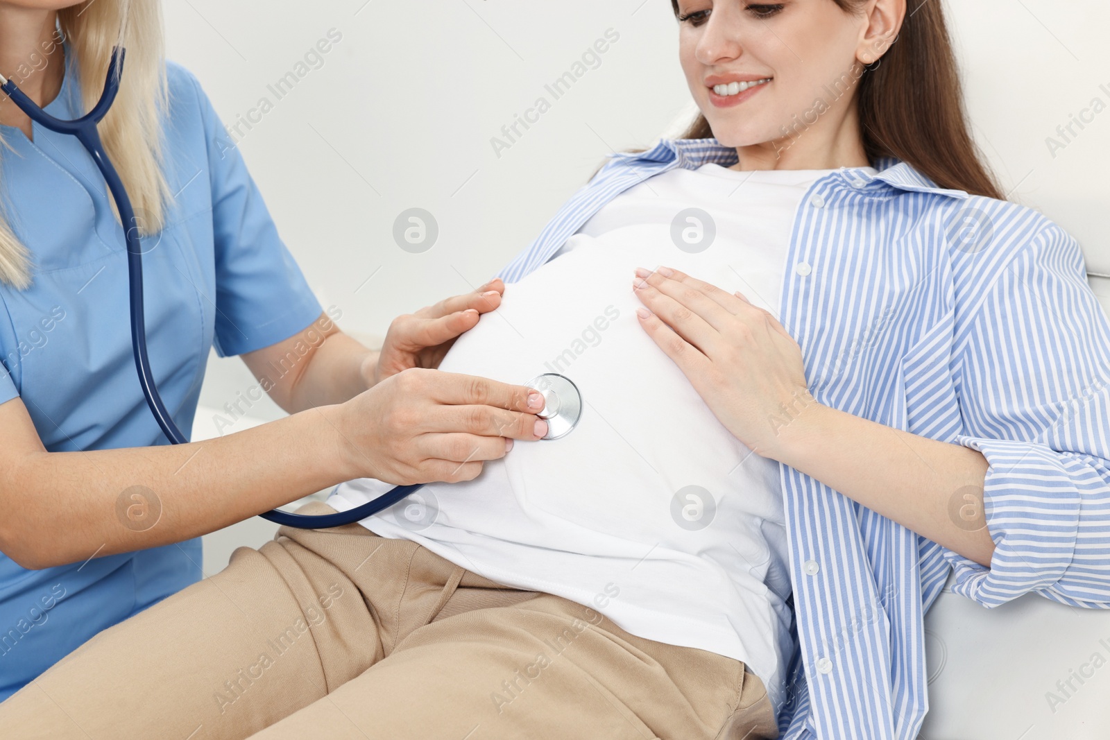 Photo of Pregnancy checkup. Doctor with stethoscope listening baby's heartbeat in patient's tummy in clinic, closeup