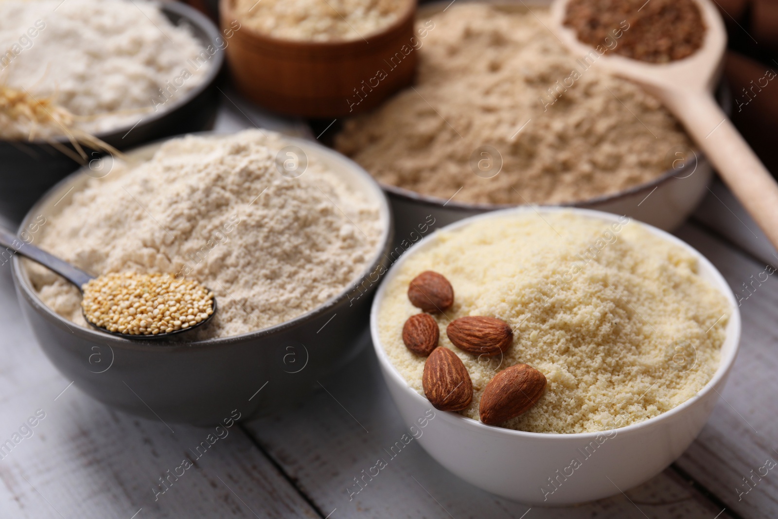 Photo of Bowls with different types of flour and ingredients on white wooden table, closeup